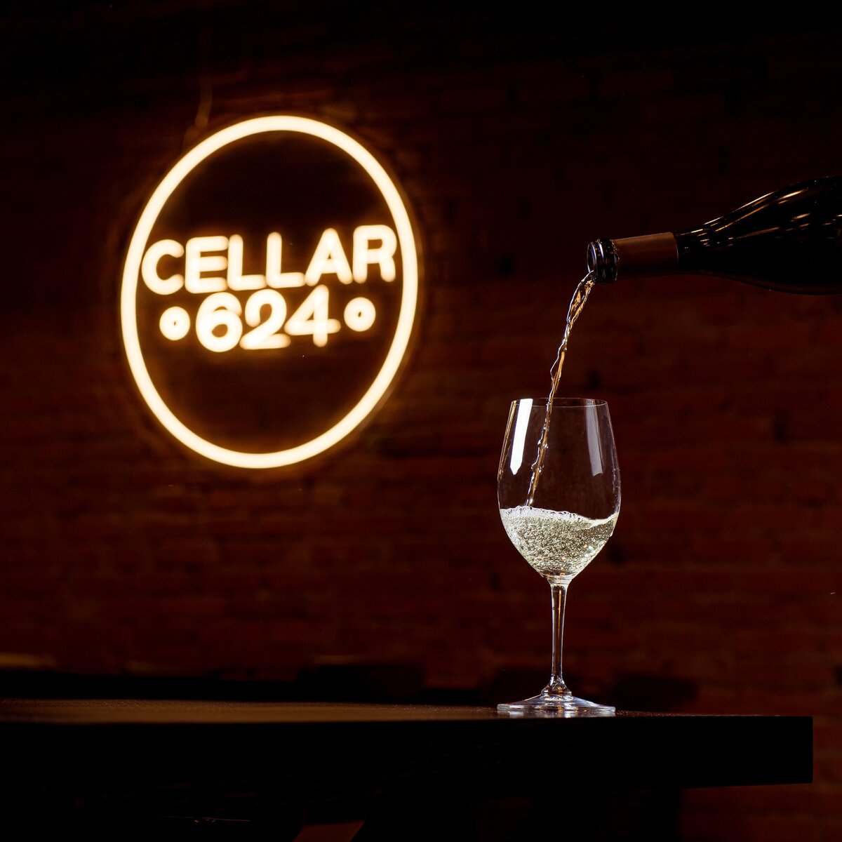 a glass of white whine being poured near a neon sign