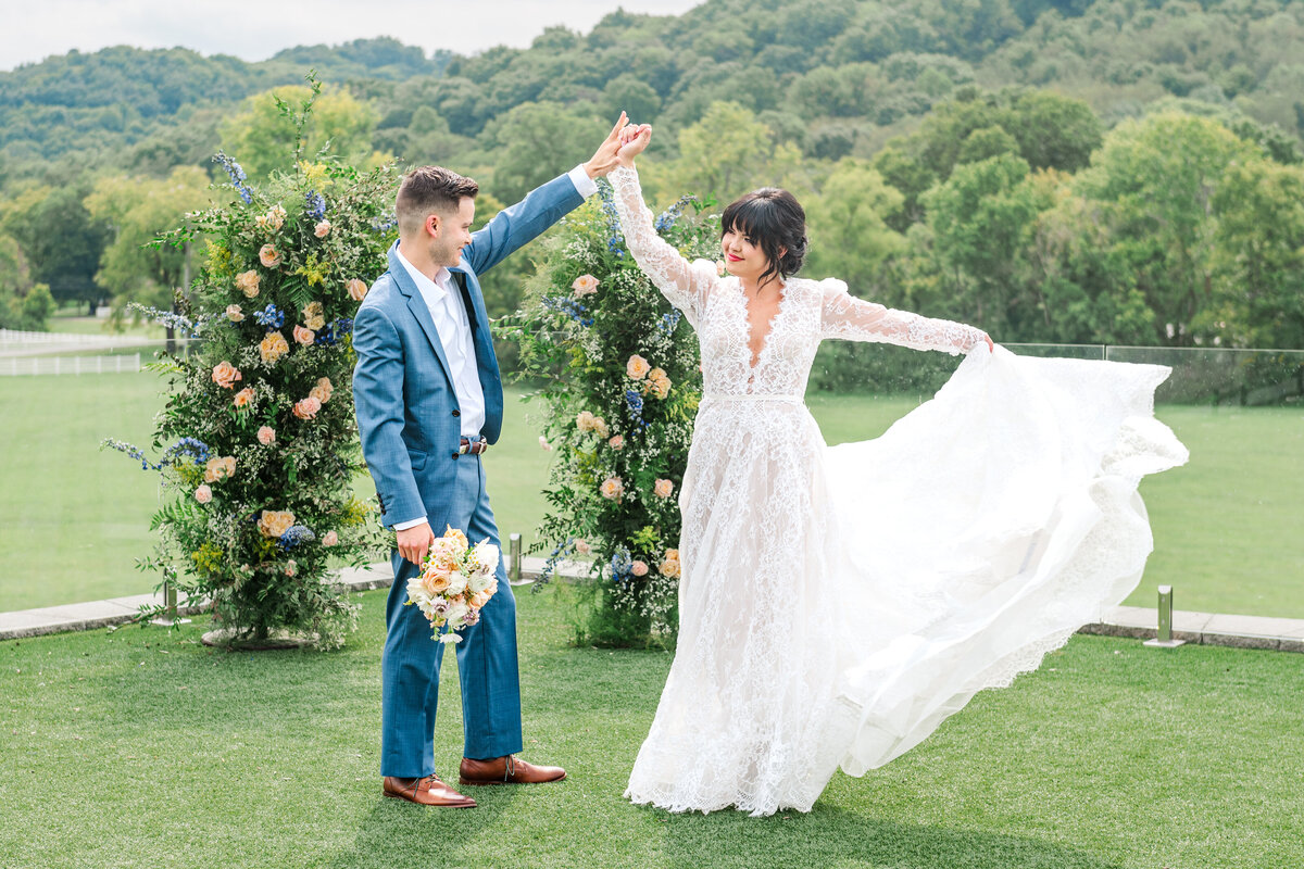 Bride showing off her dress against an overlook with flowers