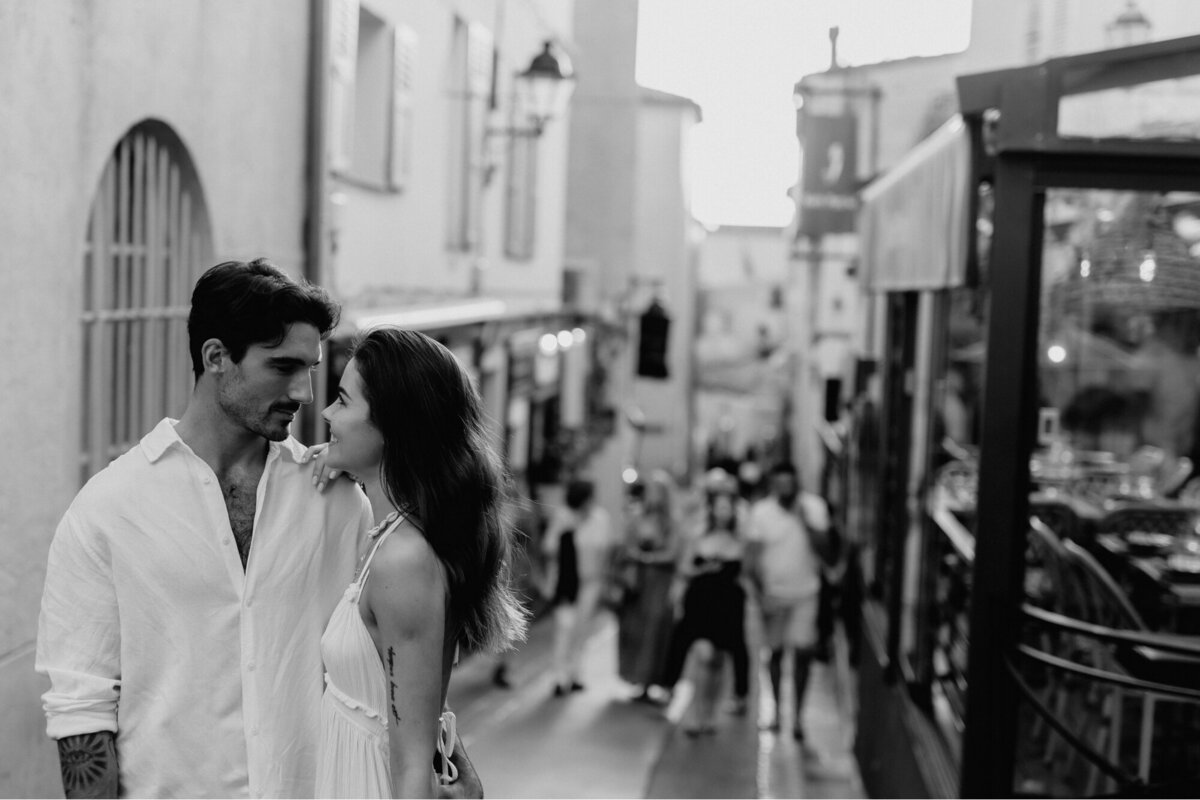 Black and white photo of Couple loving looking at one another while a busy street in France is in the background.