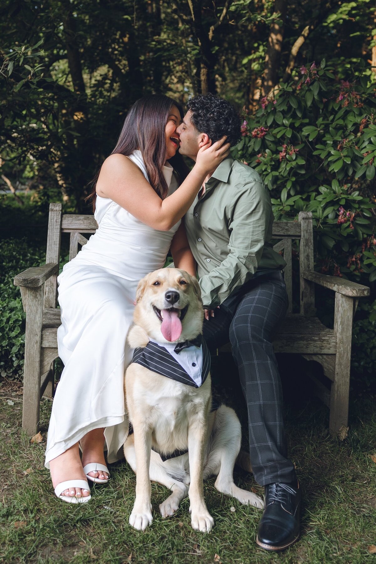 Couple cuddling on a bench with their dog nearby.
