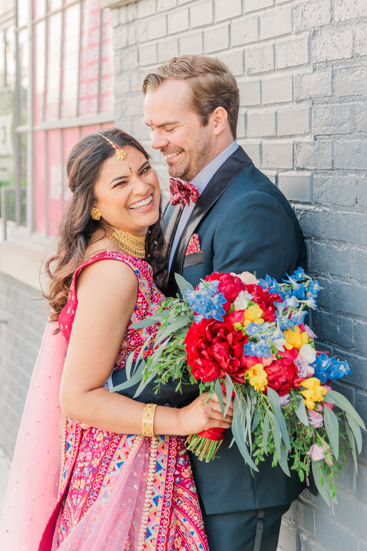 bride in vibrant pink dress holding colorful flowers and laughing