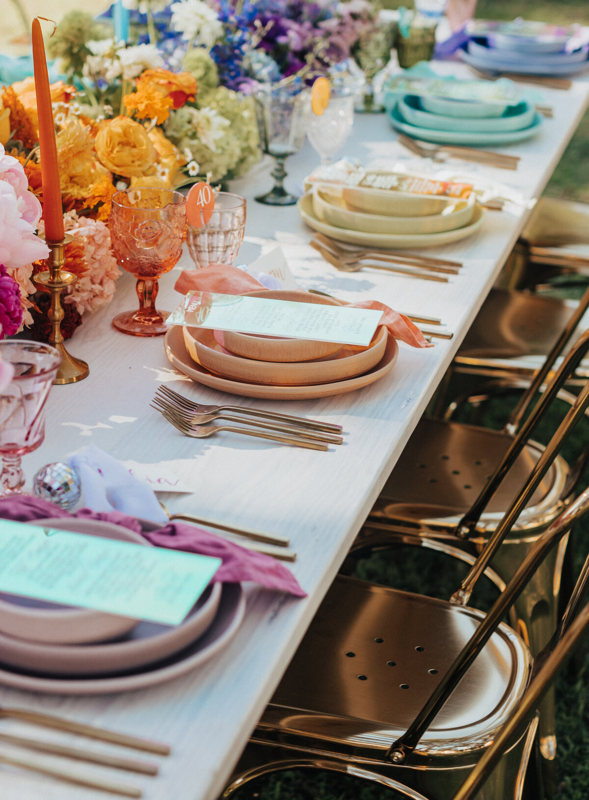 A richly styled outdoor tablescape featuring layered pastel dishware, vibrant spring florals, gold flatware, and rainbow-colored glasses. Perfectly styled for a chic garden party in Greenville, South Carolina. Captured by Dani Lacey Photographs.