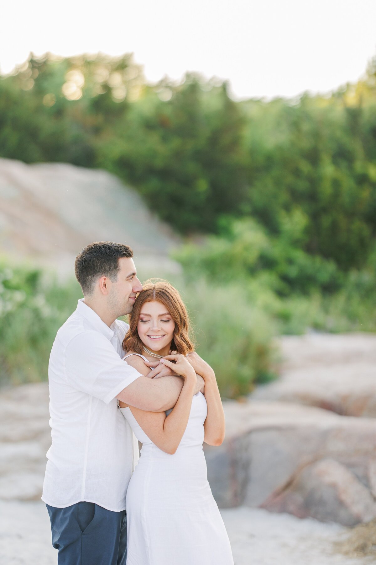 A couple snuggling and smiling during their Gloucester engagement photos at Wingaersheek Beach