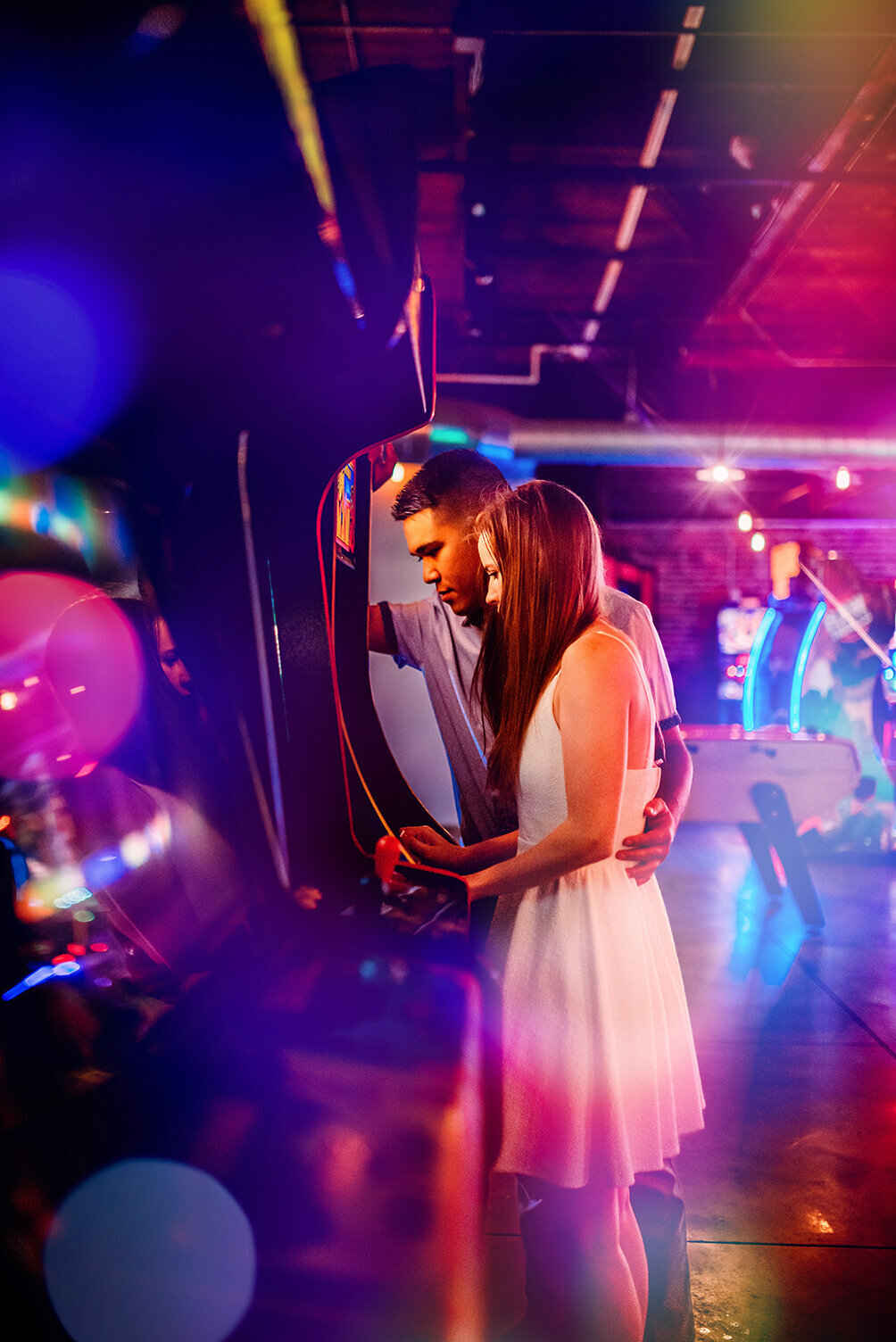 an engaged couple having a photoshoot inside an arcade, playing an arcade game