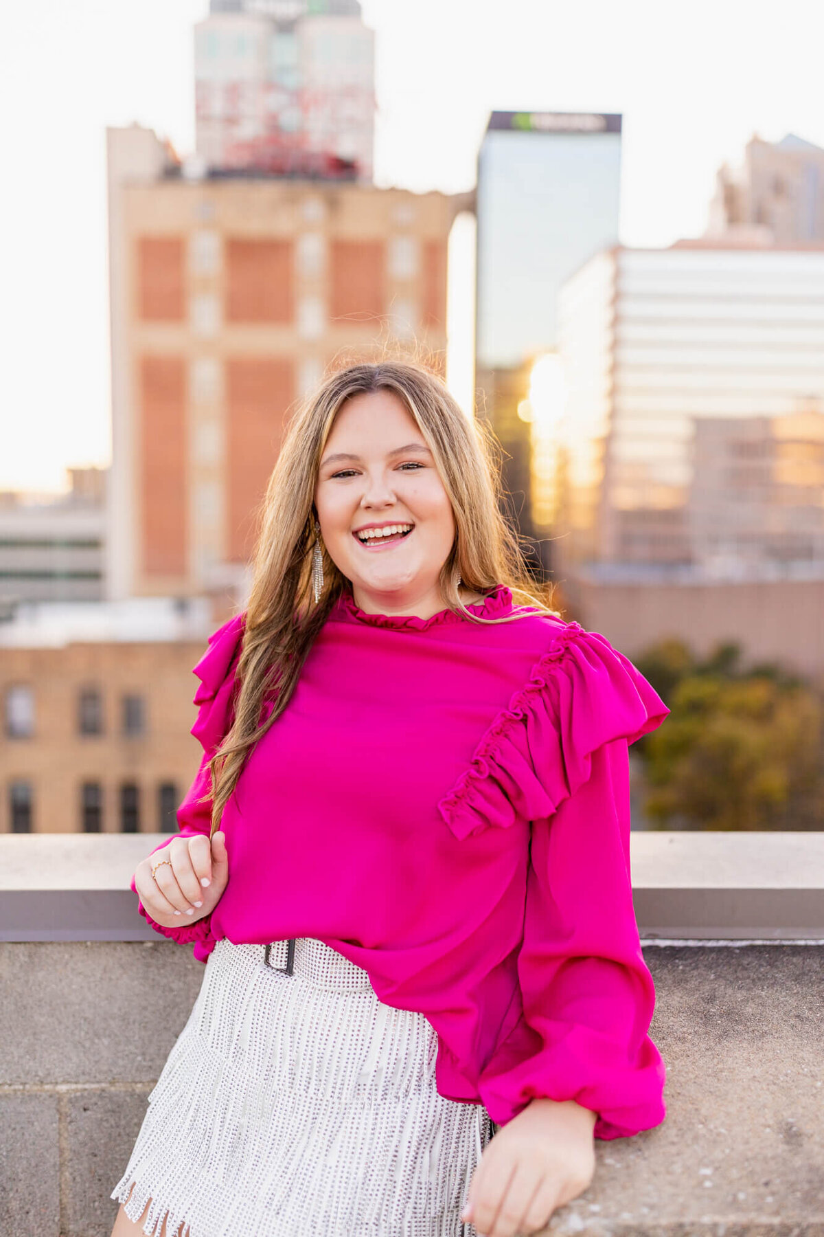 Senior girl on top of a parking garage downtown in a bright pink top and fringe bottoms