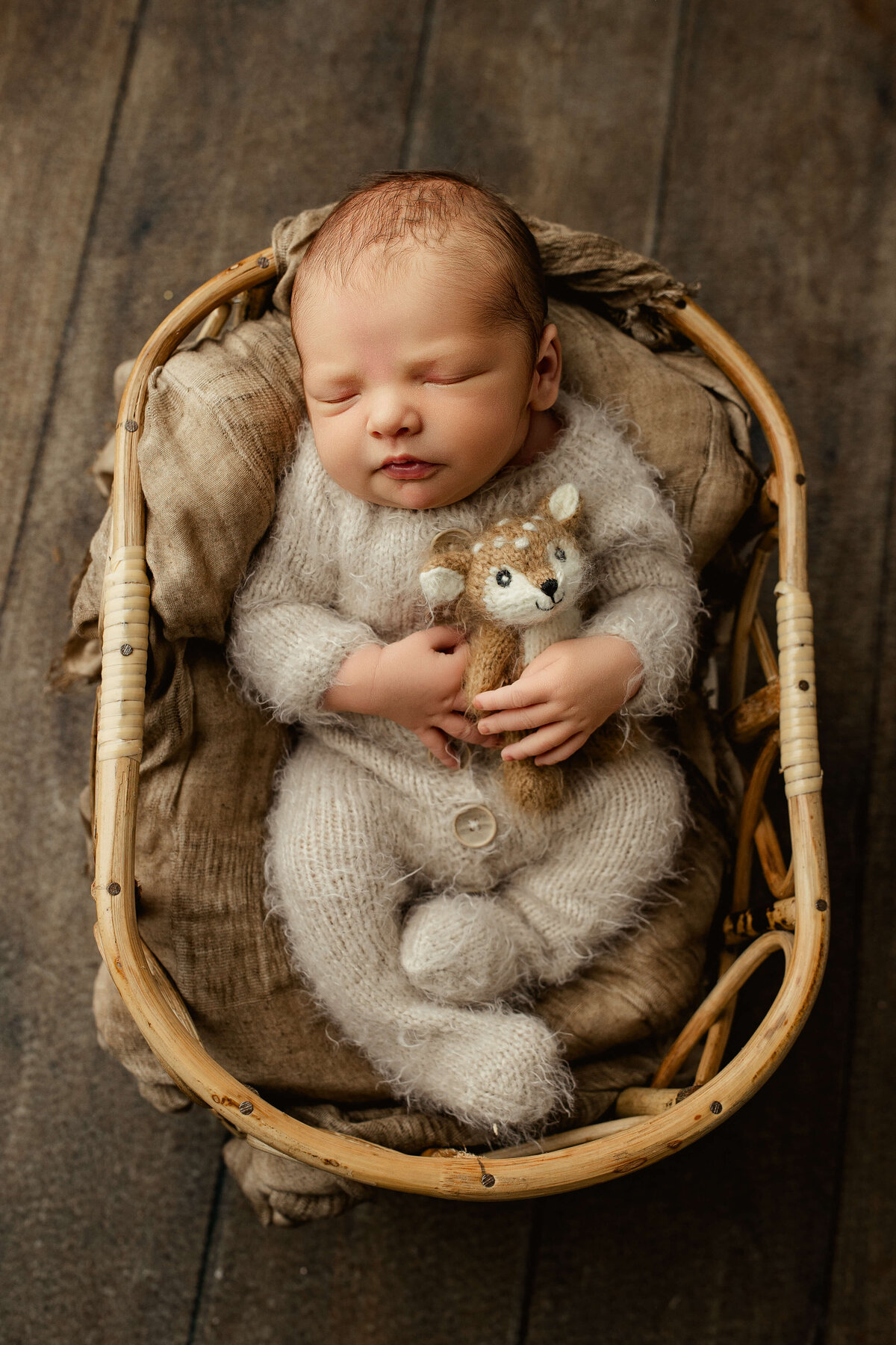 sleeping baby boy in a fuzzy neutral colored knit romper holding a tiny stuffed deer during newborn photos 