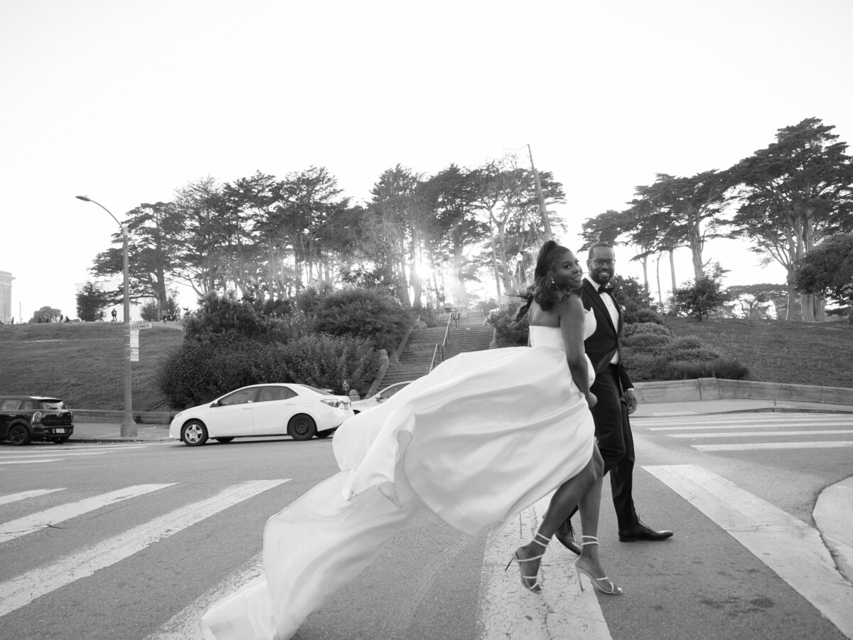 black wedding couple walking in alamo square, the  groom is in a tux and the bride is wearing a white dramatic bridal gown