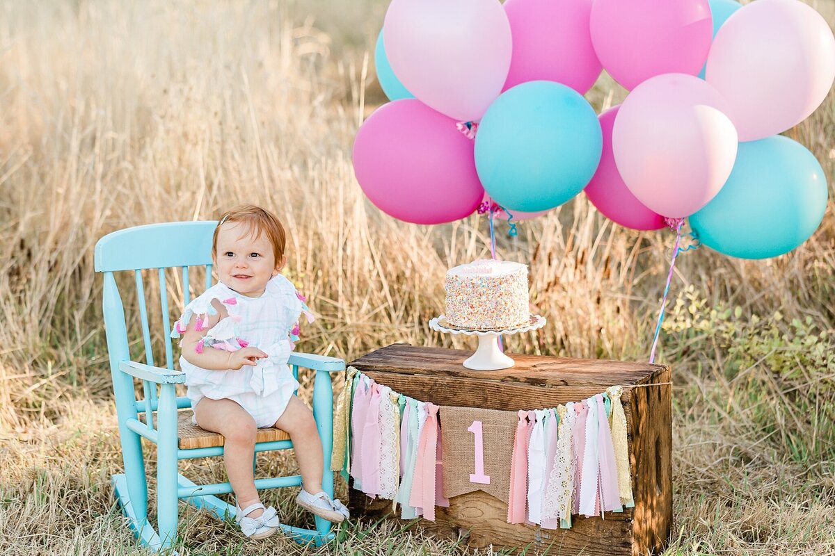 baby girl in rocking chair with pink and blue balloons