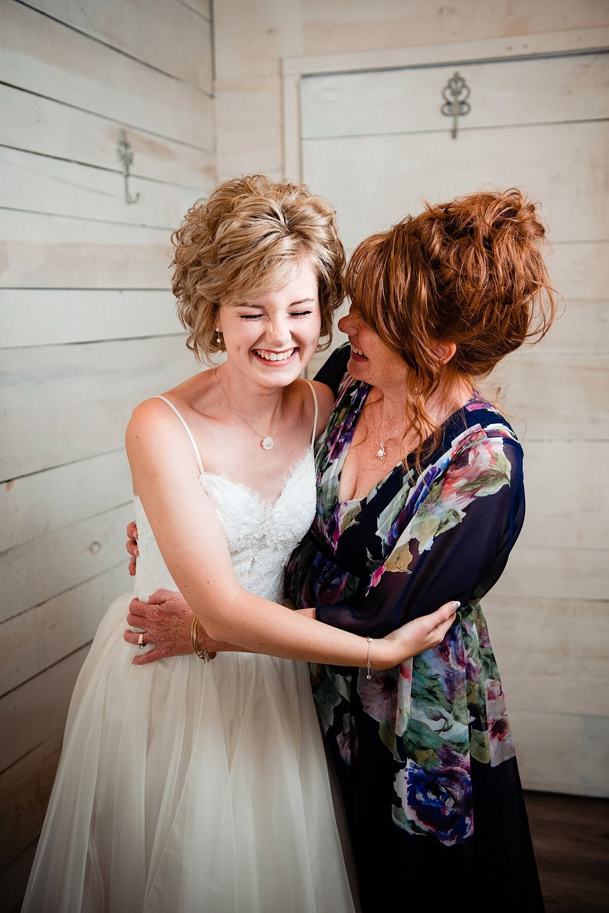 Mother hugging her daughter and sharing a laugh while getting into her wedding dress