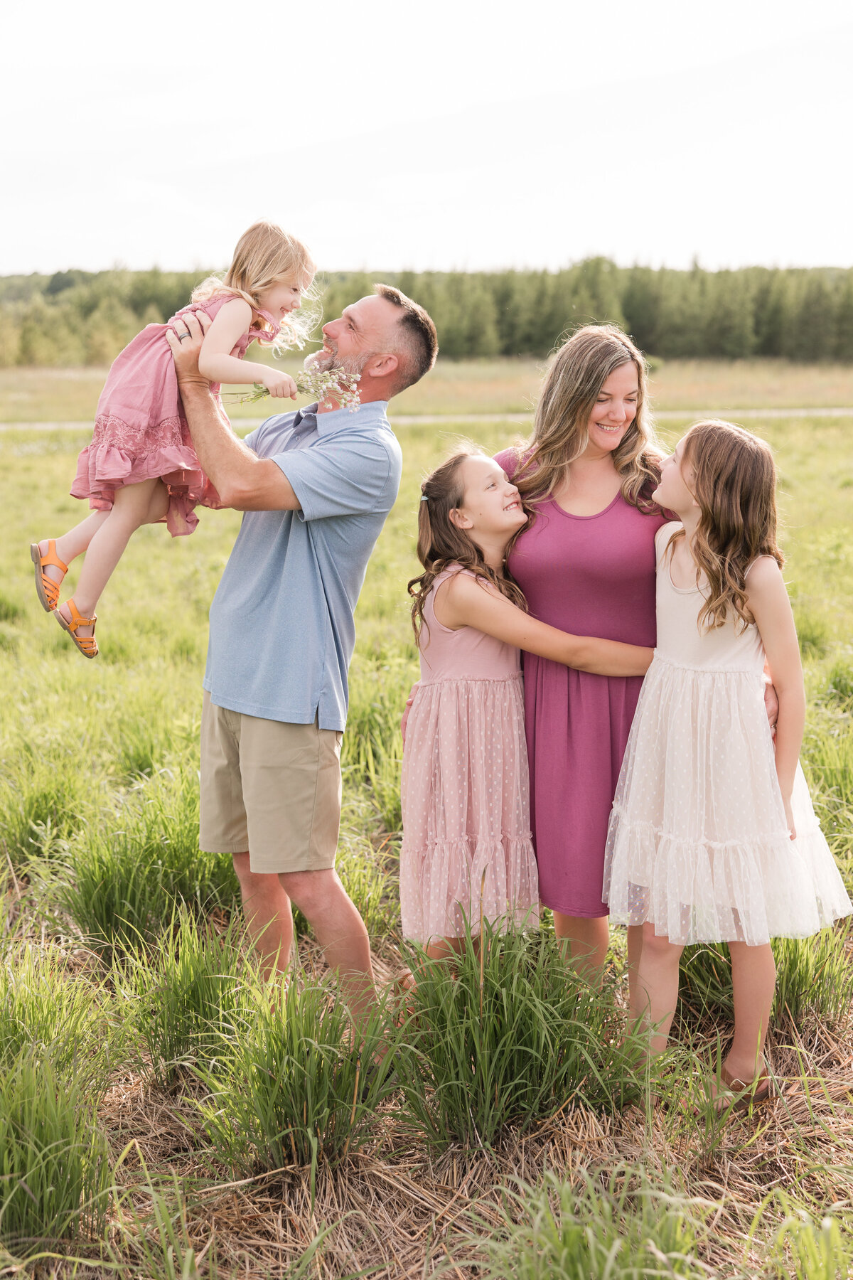 A family is standing in a field and interacting with one another lovingly