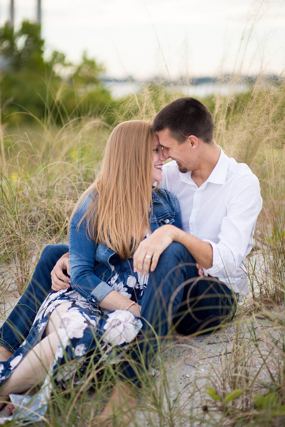Natural light couple sitting on the beach in the sand and seagrass while staring at each other. Captured by Sarah Wyndham Photography at Apollo Beach Preserve 