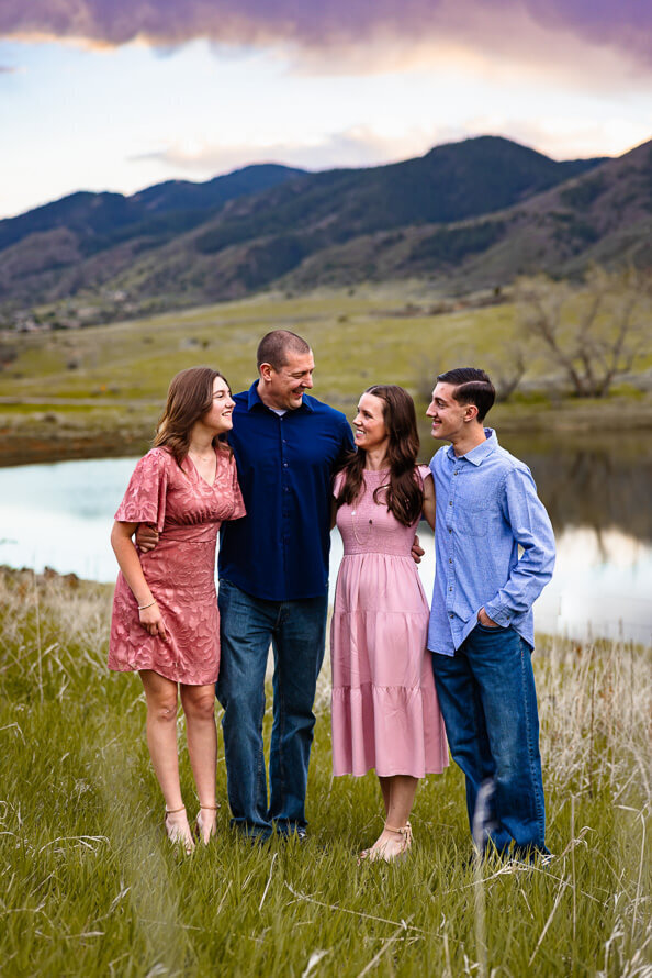 A family of four laughs together in front of a lake at South Valley Park in the Ken Caryn Valley.