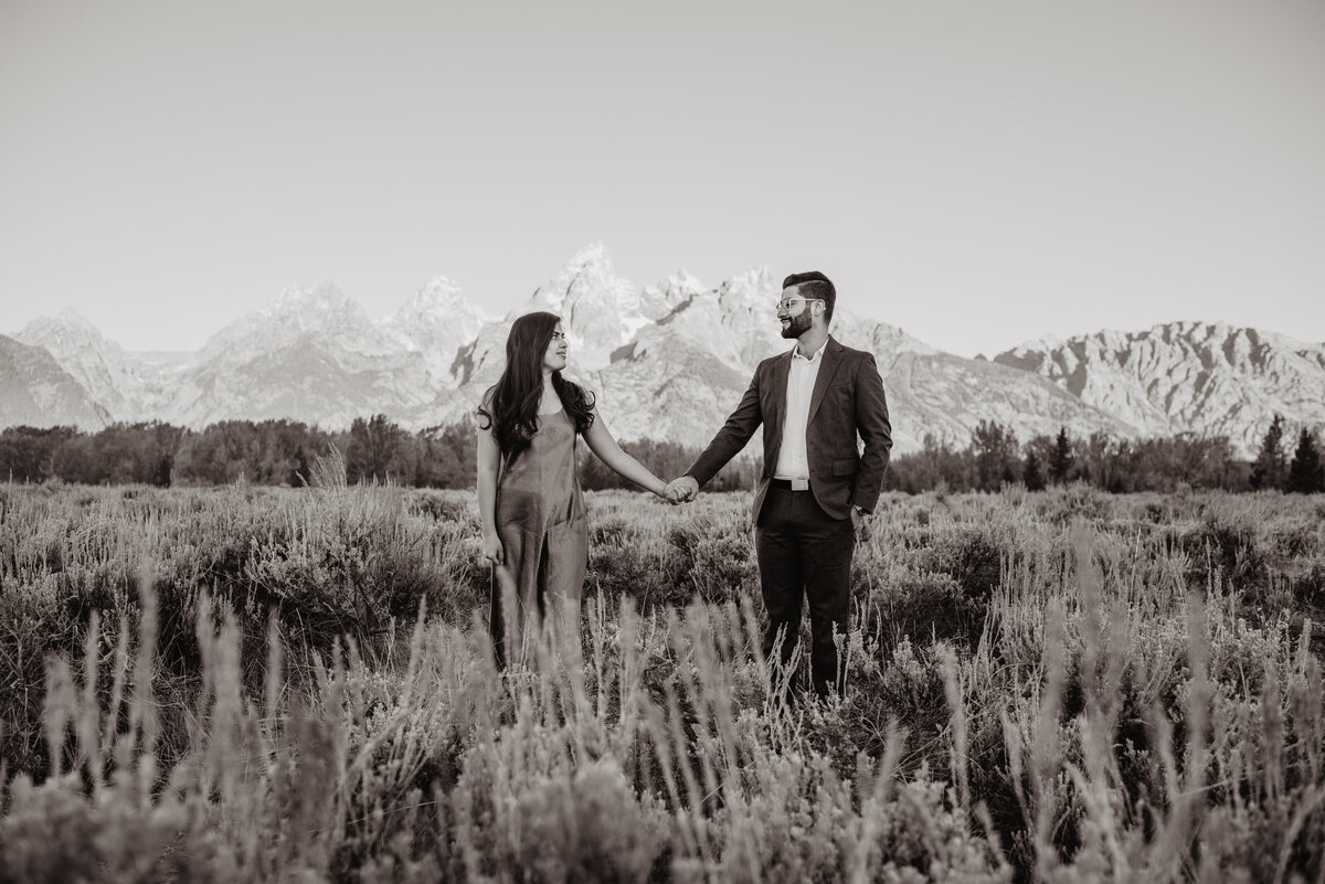 photographers in jackson hole photographs black and white photo of man and woman holding hands in a field while looking at each other for their fall engagement session