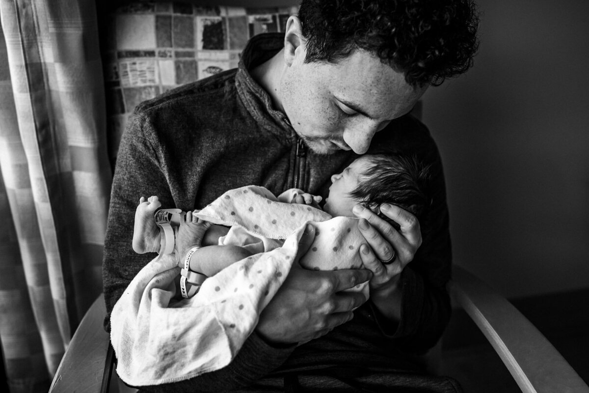 dad holding newborn draped in blanket close to his face with eyes closed