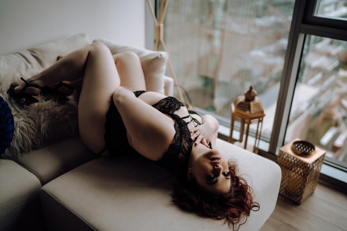 Curvy red haired woman posing laying on taupe couch