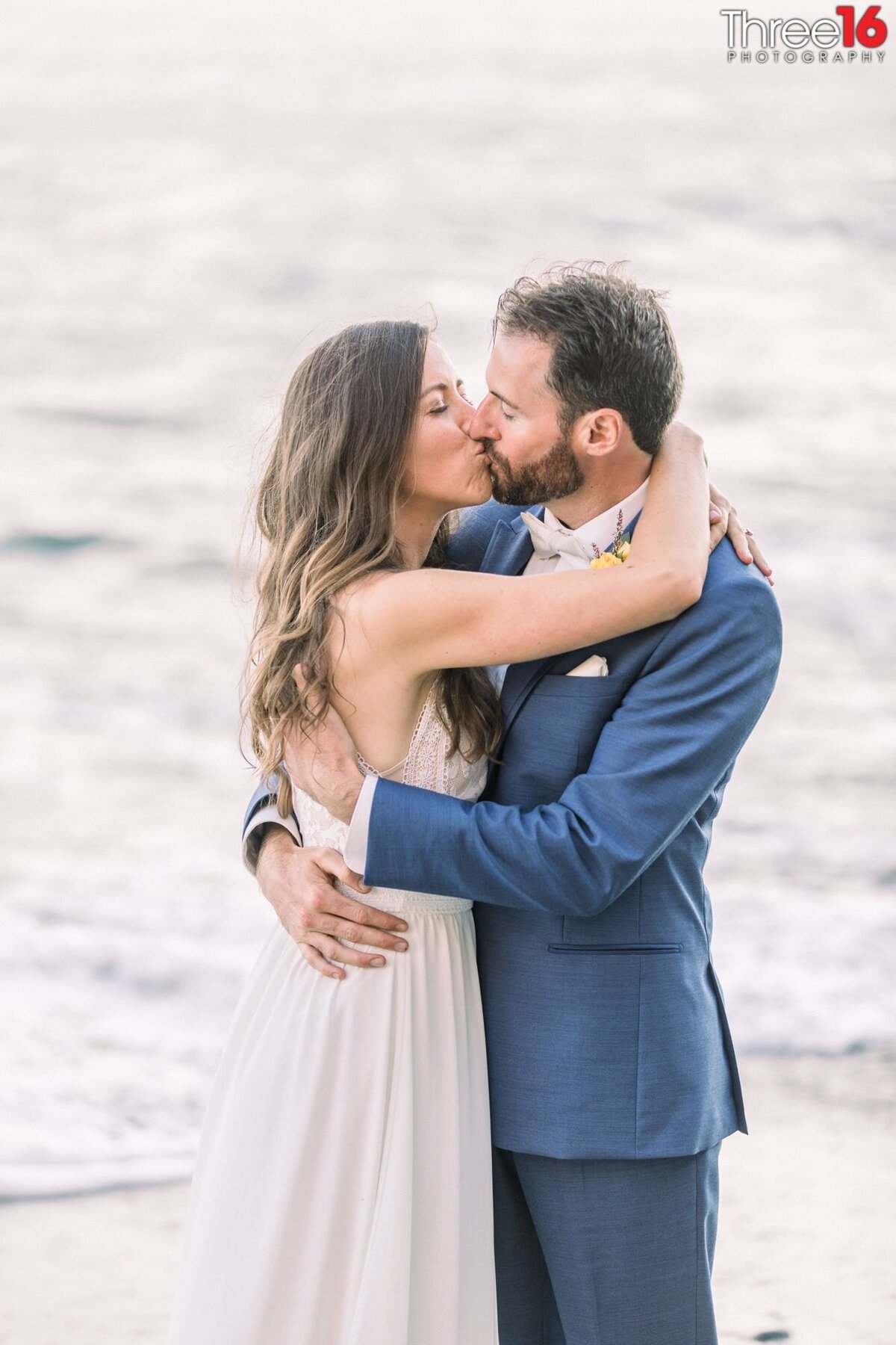 New husband and wife share a passionate kiss on the beach near the ocean waters