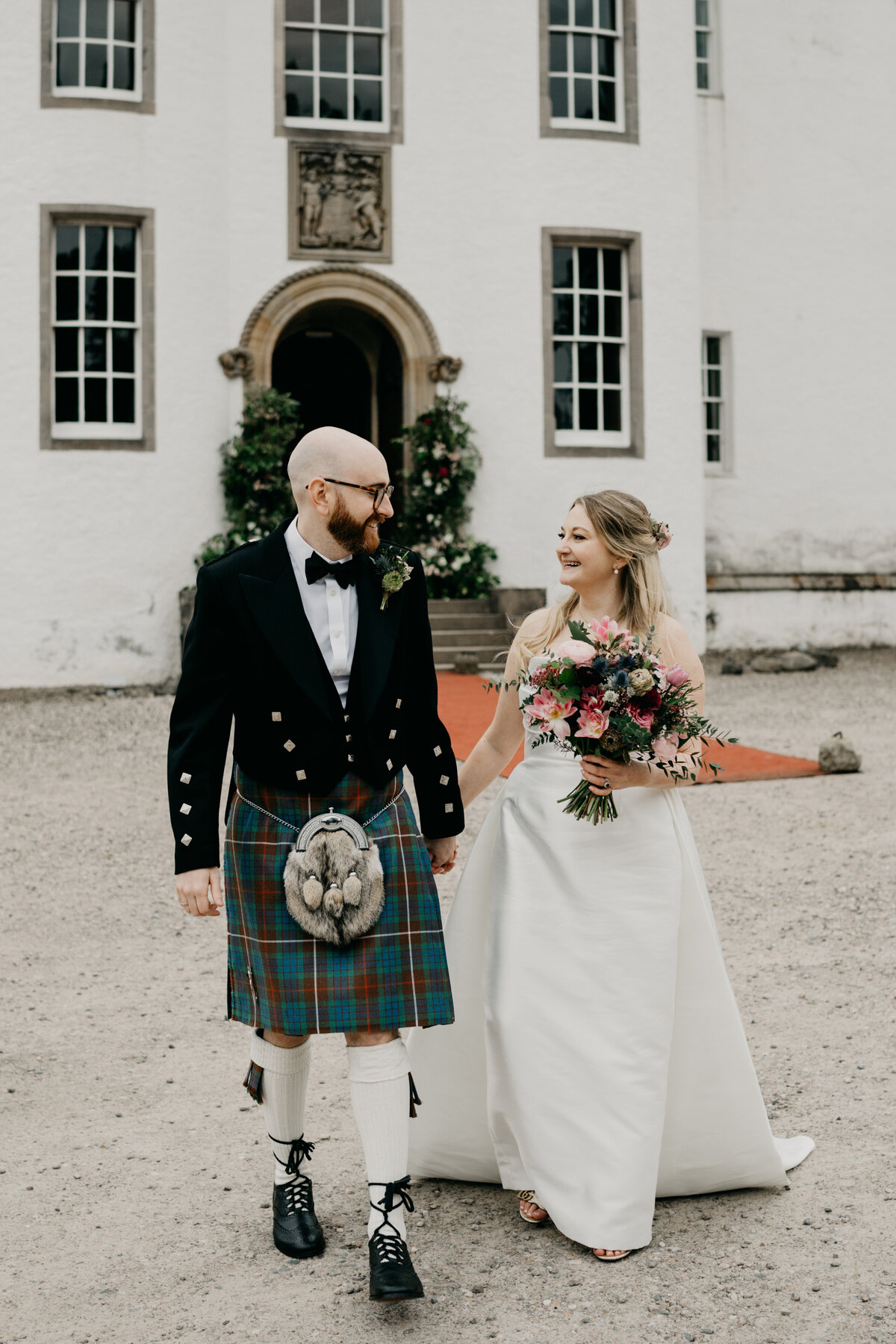 A bride and groom walk hand in hand for photography outside Blair Castle in Perthshire after their wedding ceremony.