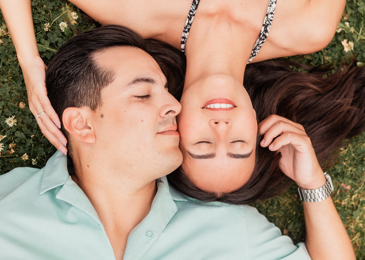 A couple laying in the grass, heads beside each other and eyes closed