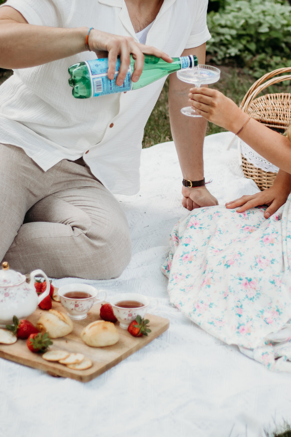 A picnic setup with strawberries and tea is set at the couple pours a glass of sparkling water during their session with a Duluth wedding photographer, S Jacobson Photography.