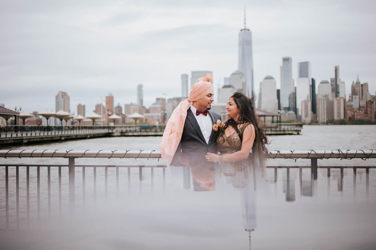A couple embraces along the waterfront with the New York City skyline in the background during their New Jersey engagement session