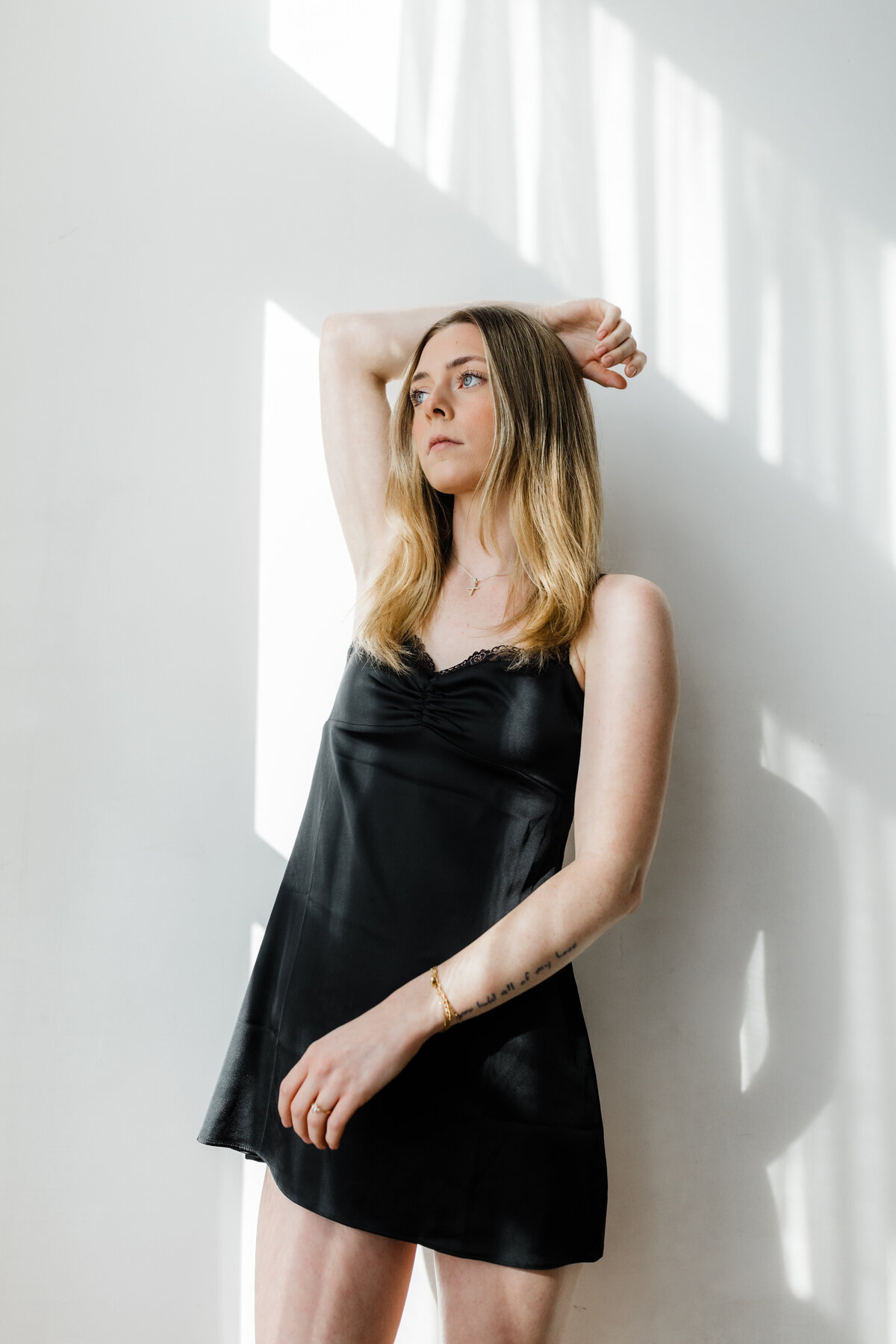 Woman posing in natural light, wearing a black dress with confidence during a South Bend boudoir session.