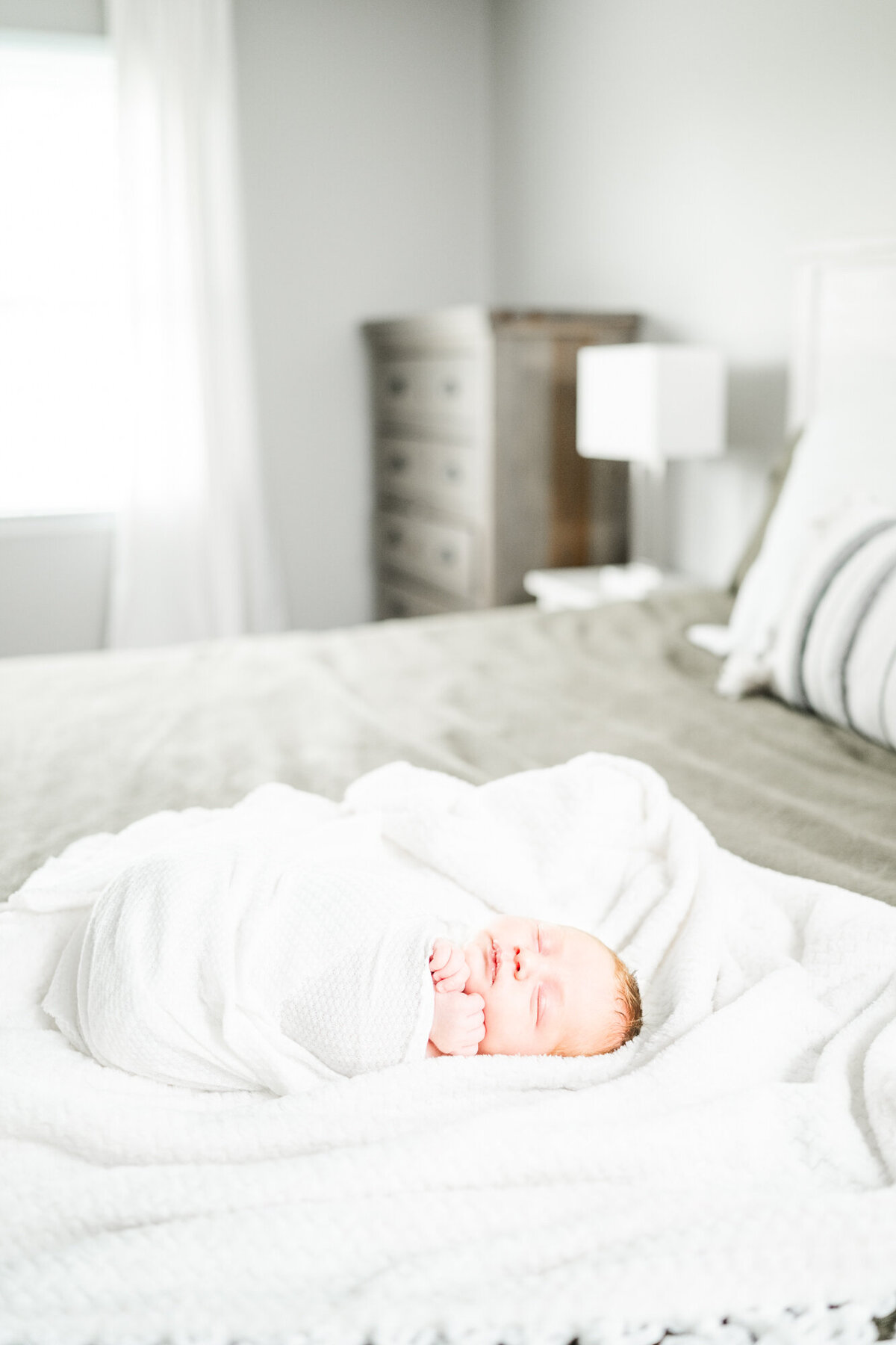 Newborn baby laying on a ben wrapped in a white blanket during his lifestyle newborn session in New Jersey