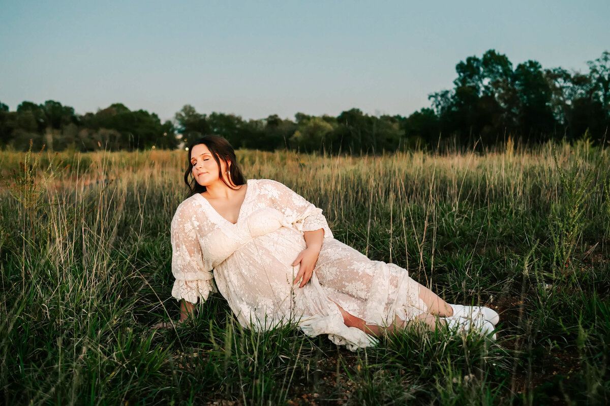 maternity photo in Branson of mom holding baby bump sitting in grass