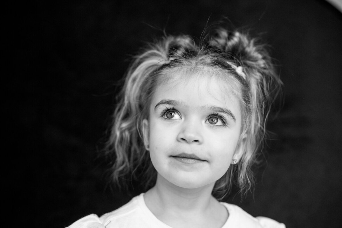 Black and white image of a young girl with pigtails looking past the camera with a faint smile and bright eyes for school pictures