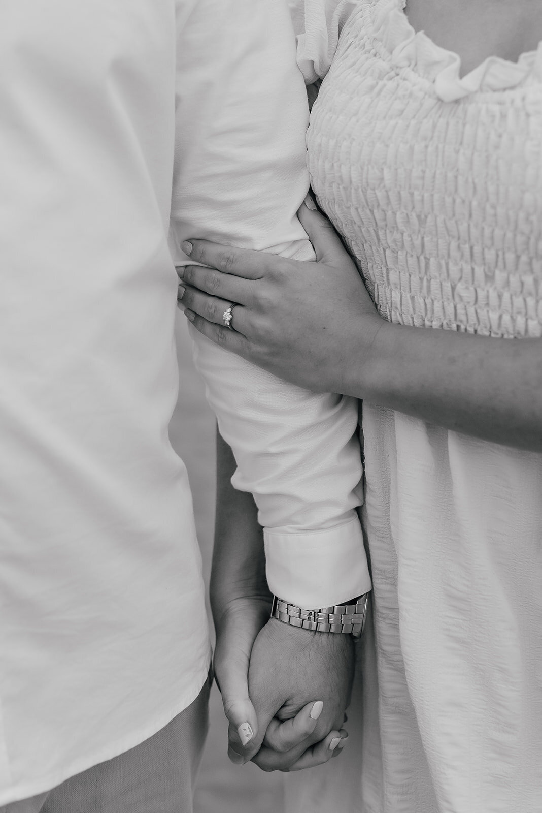 Close up of engagement ring as female softly holds fiance's arm 