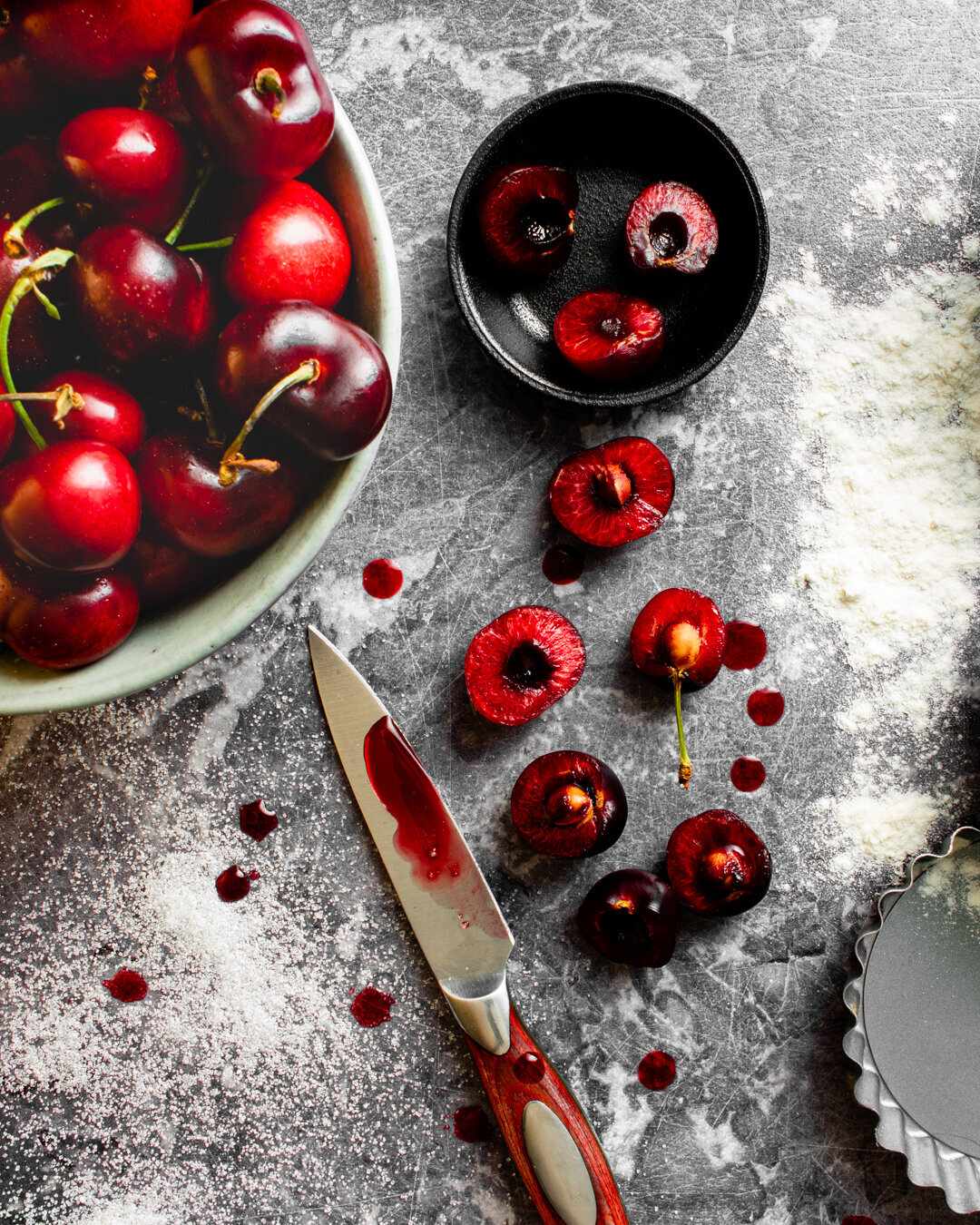 A bowl of cherries with some cut cherries on a work top with a knife