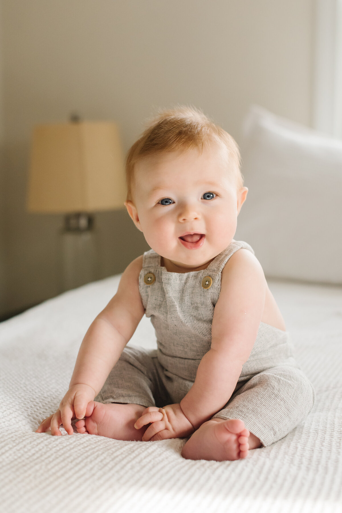 Six month old child in overalls sitting up on bed - Northern Virginia family photographer