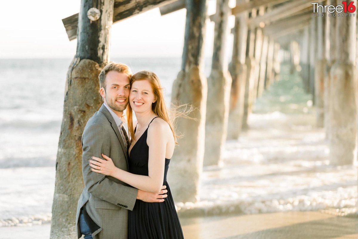 Engaged couple pose together for photos under the Newport Beach Pier's wooden structure