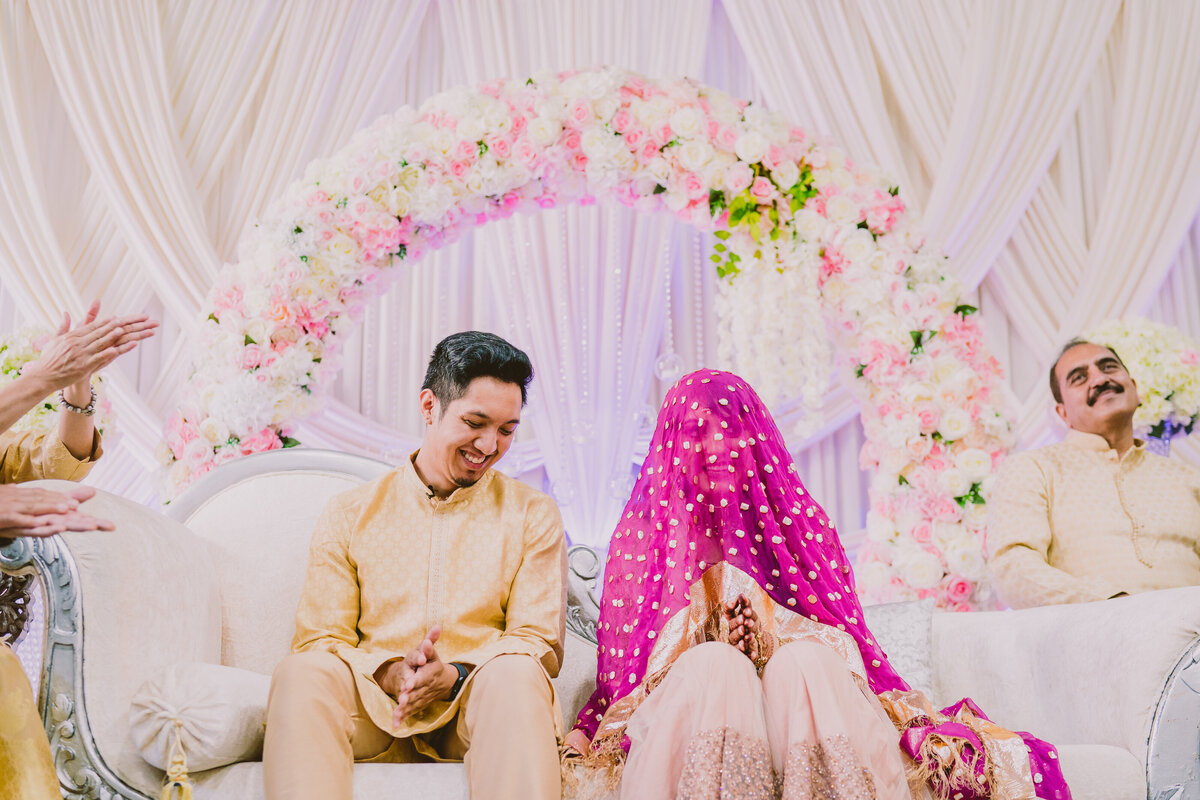 A muslim bride with a veil over head laughing with the groom during the nikkah wedding ceremony