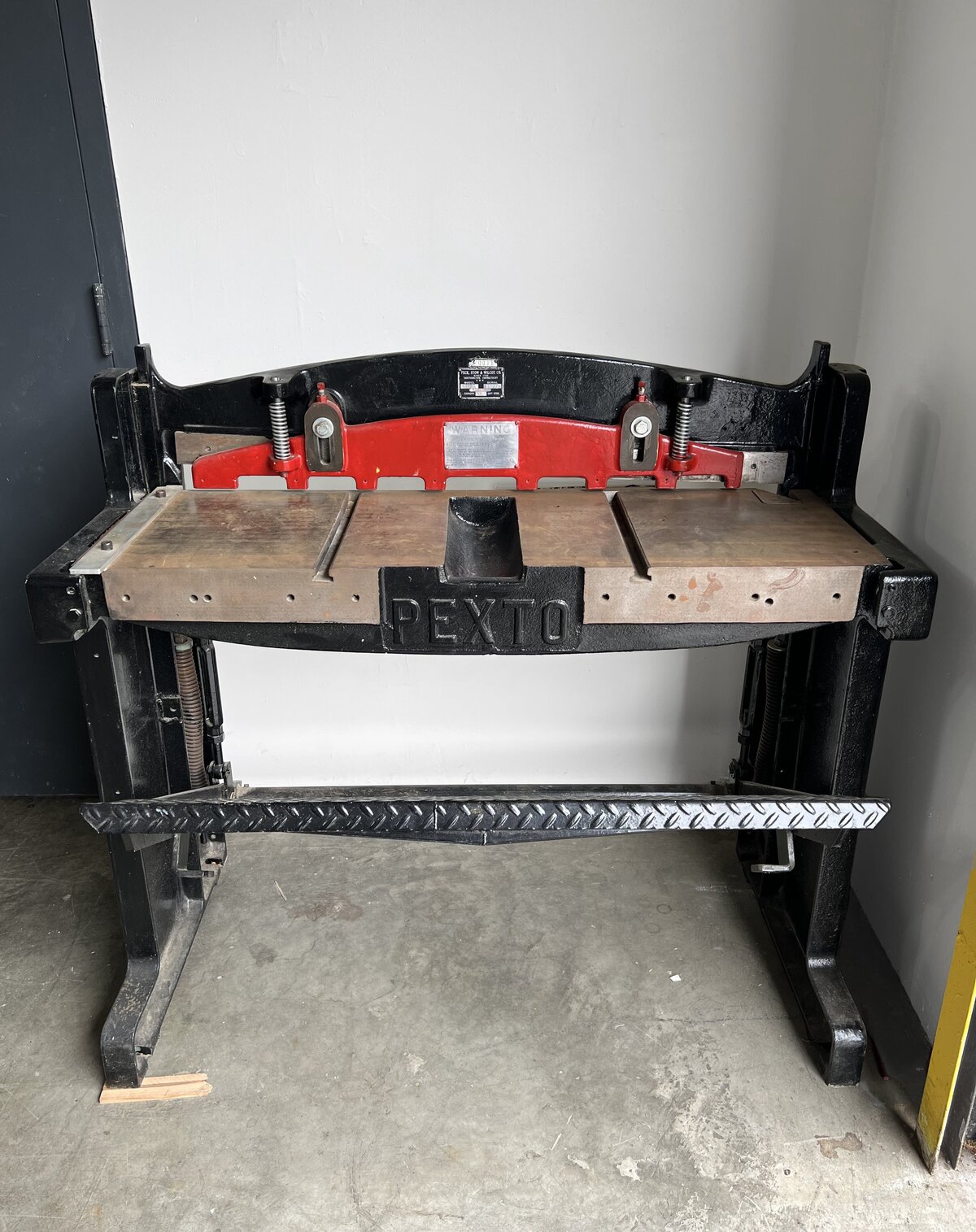 A robust metal plate cutter, labeled "PEXTO," used for cutting and preparing metal plates in a professional printmaking studio.