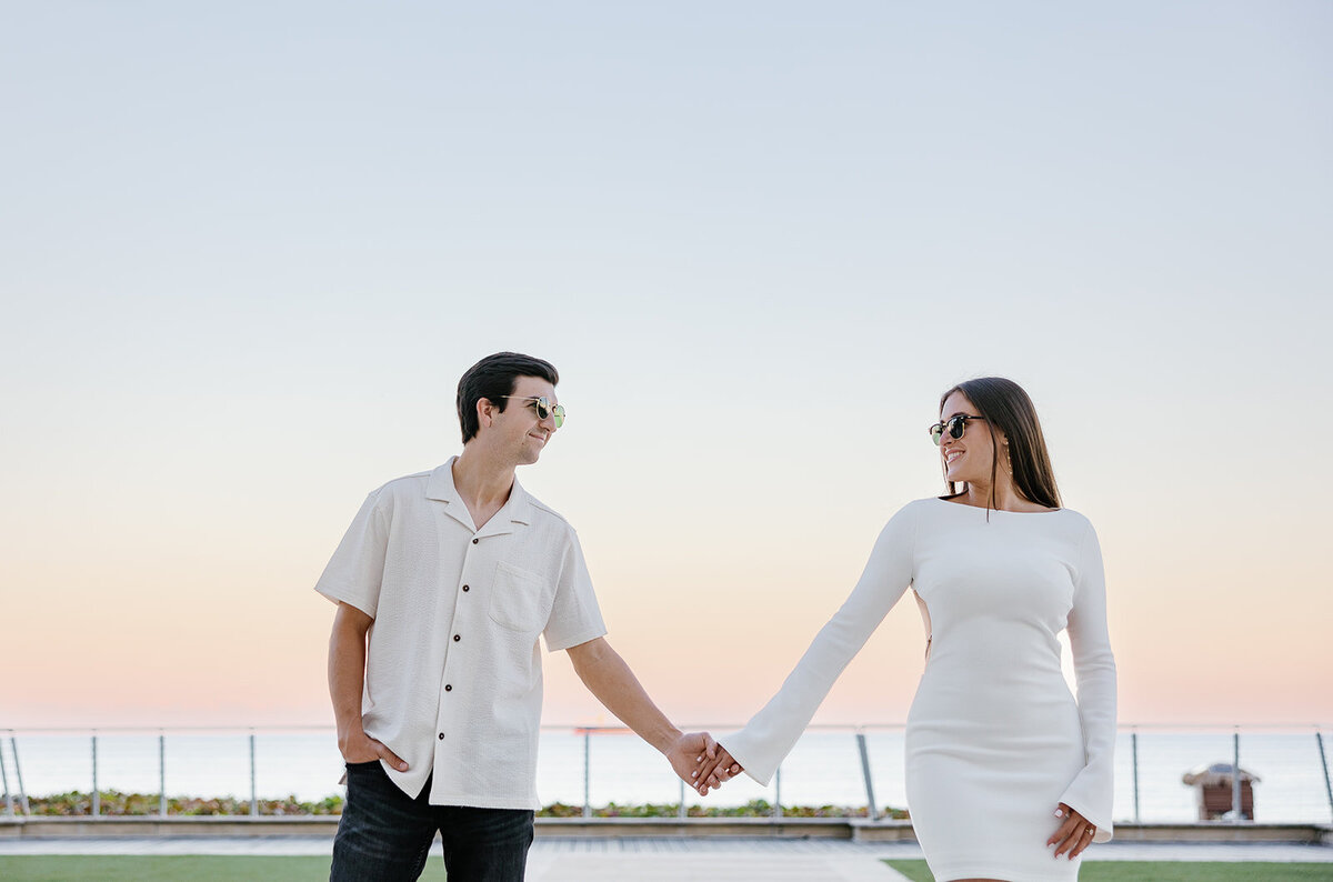 Rebecca and Graysen laugh as they hold hands at the water’s edge, creating joyful memories during their romantic engagement session at Marriott Hotel Fort Lauderdale.