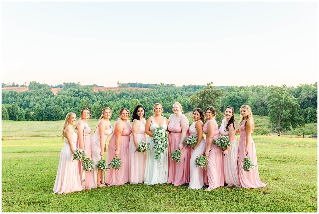 bridesmaids with bride posing in field with pink dresses on