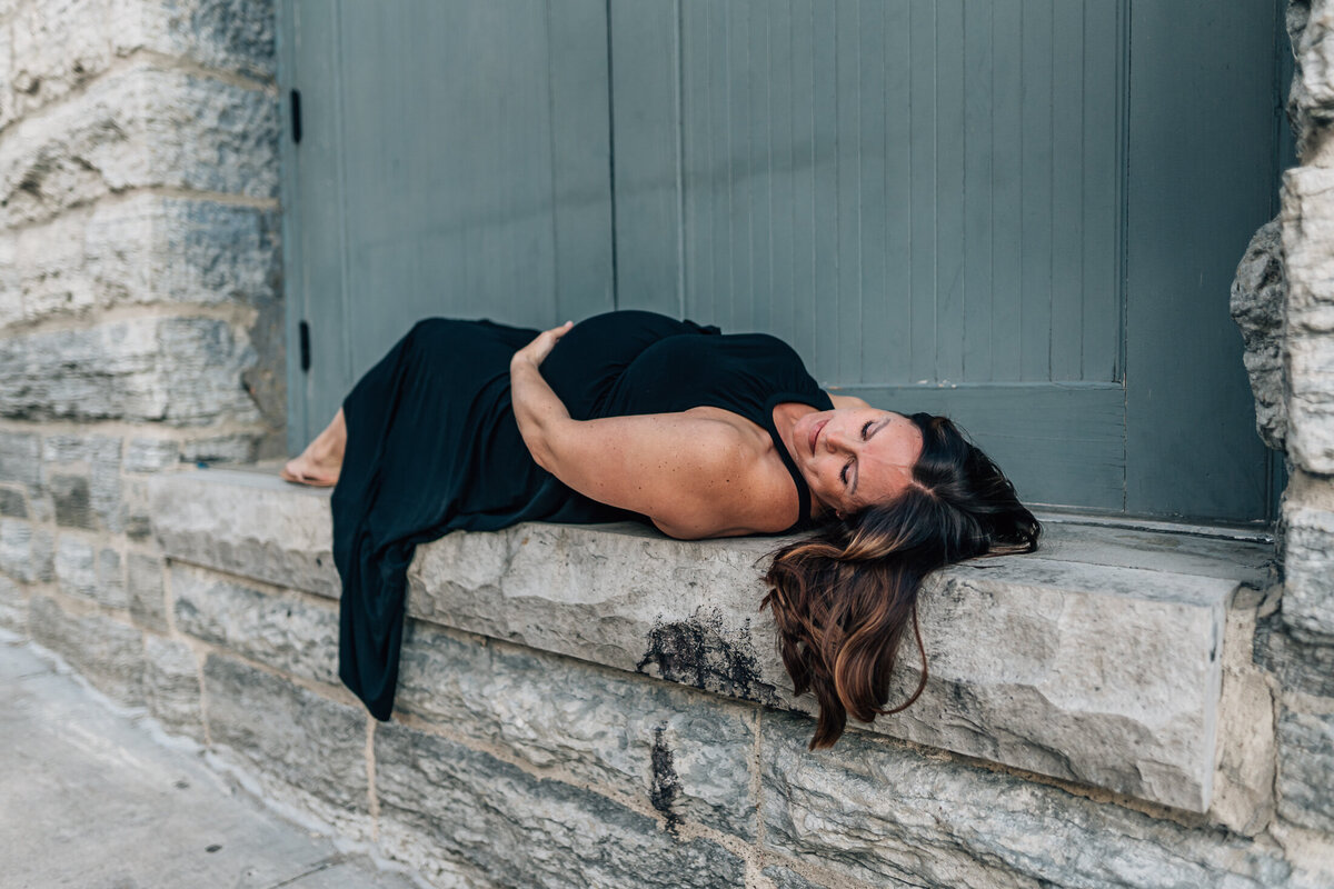 A stunning image of a pregnant mother lying with eyes closes on the doorframe ledge of a stone building near the historic Stone Arch Bridge in Minneapolis.