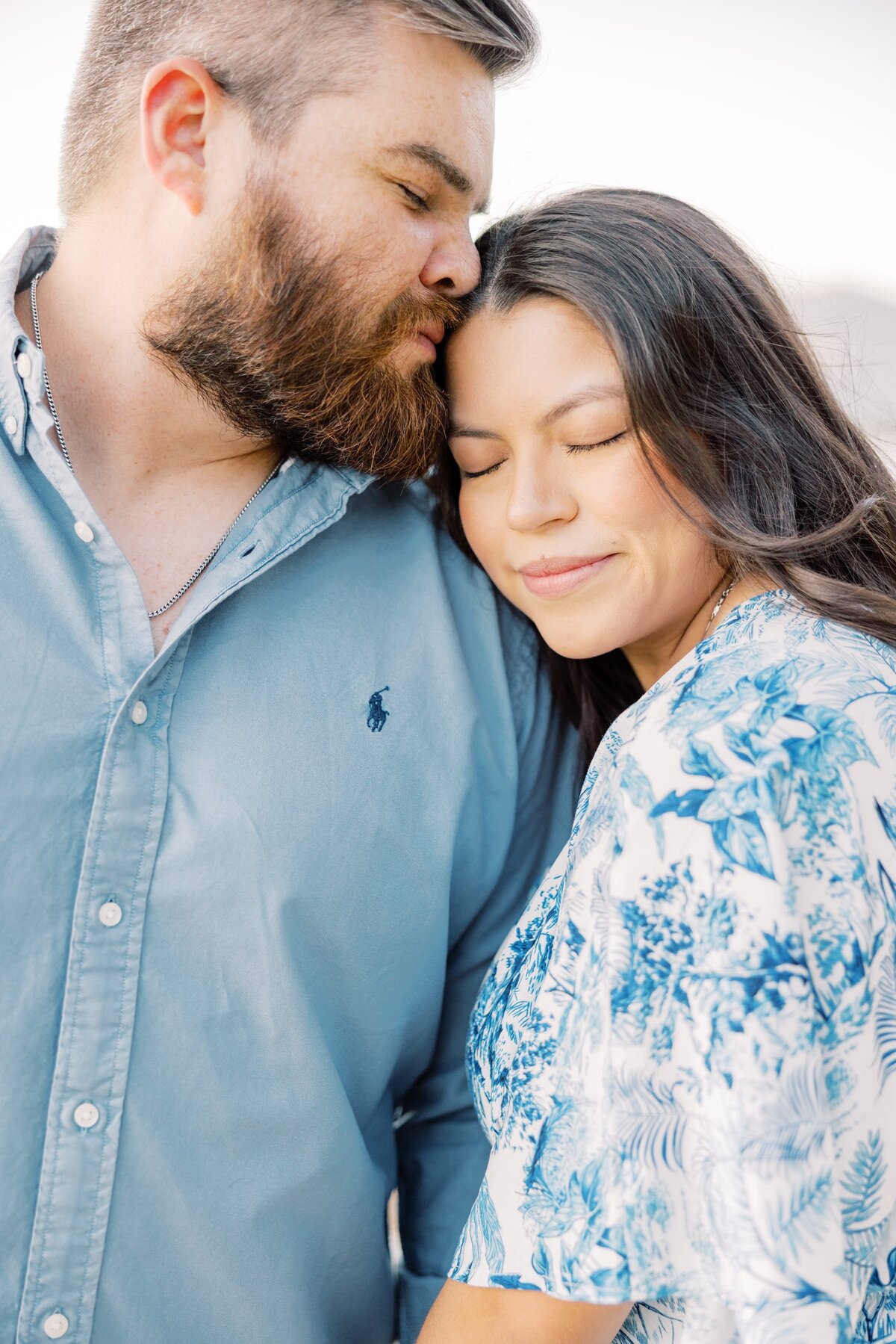 This is a close up shot of a boyfriend and girlfriend. The womans head is nestled in her boyfriends chest and her eyes are closed with a soft smile on her face while her boyfriend kisses her forehead. Taken by a local Breckenridge photographer. 