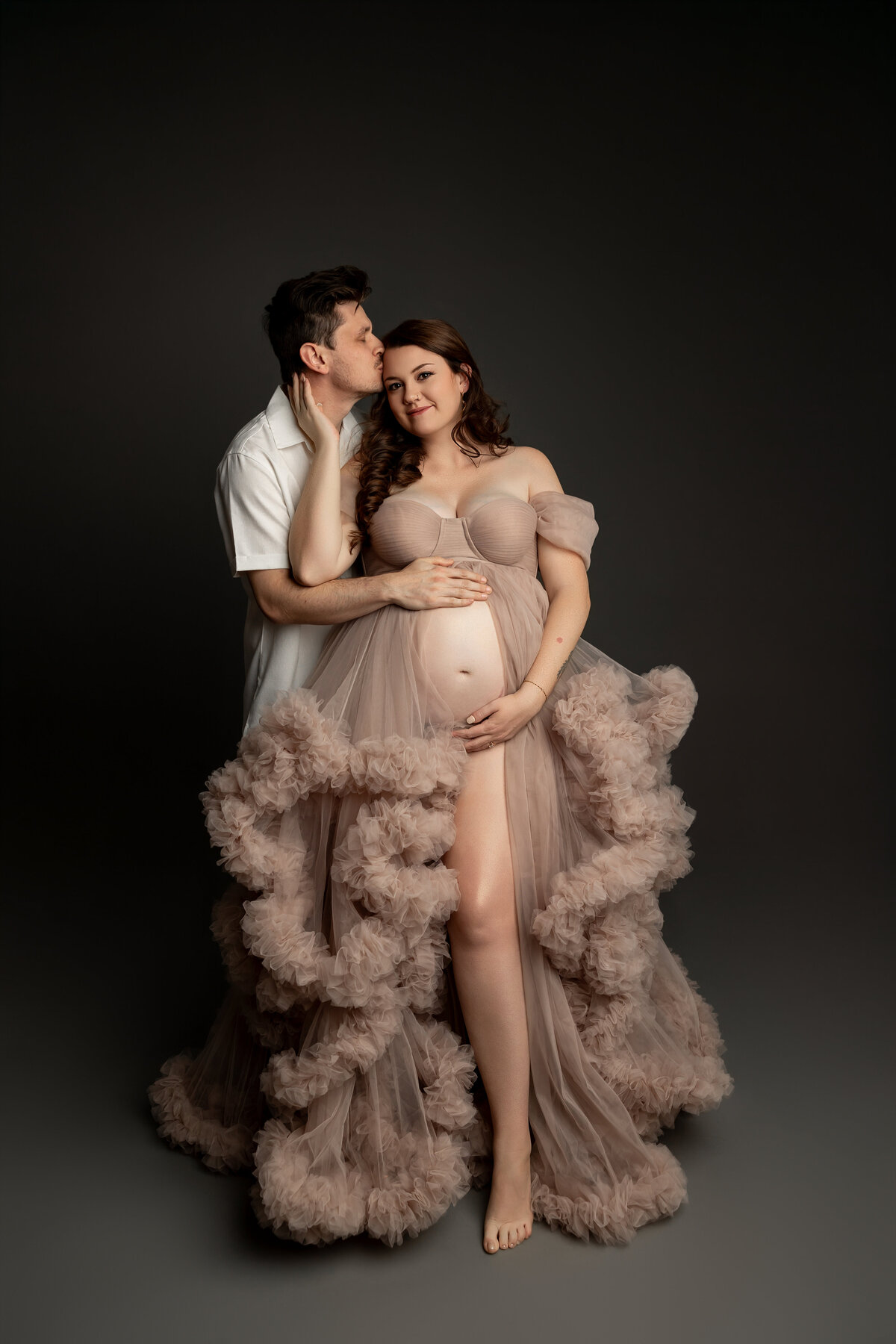 Wearing a beige dress, the expectant mother stands with her husband, both sharing a tender moment as they prepare for their new arrival. Captured by Inland Empire maternity photographer Kaitlyn Dawn Photography.