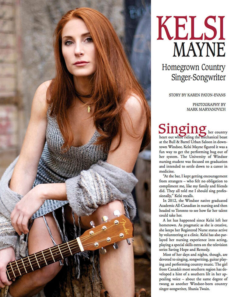 Magazine Article Windsor Life Musician Kelsi Mayne sittings against stone wall holding neck of guitar