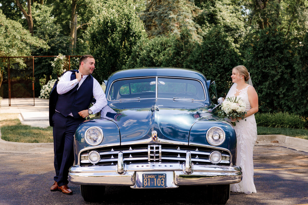 Emily and Nate gaze at each other over a vintage car.