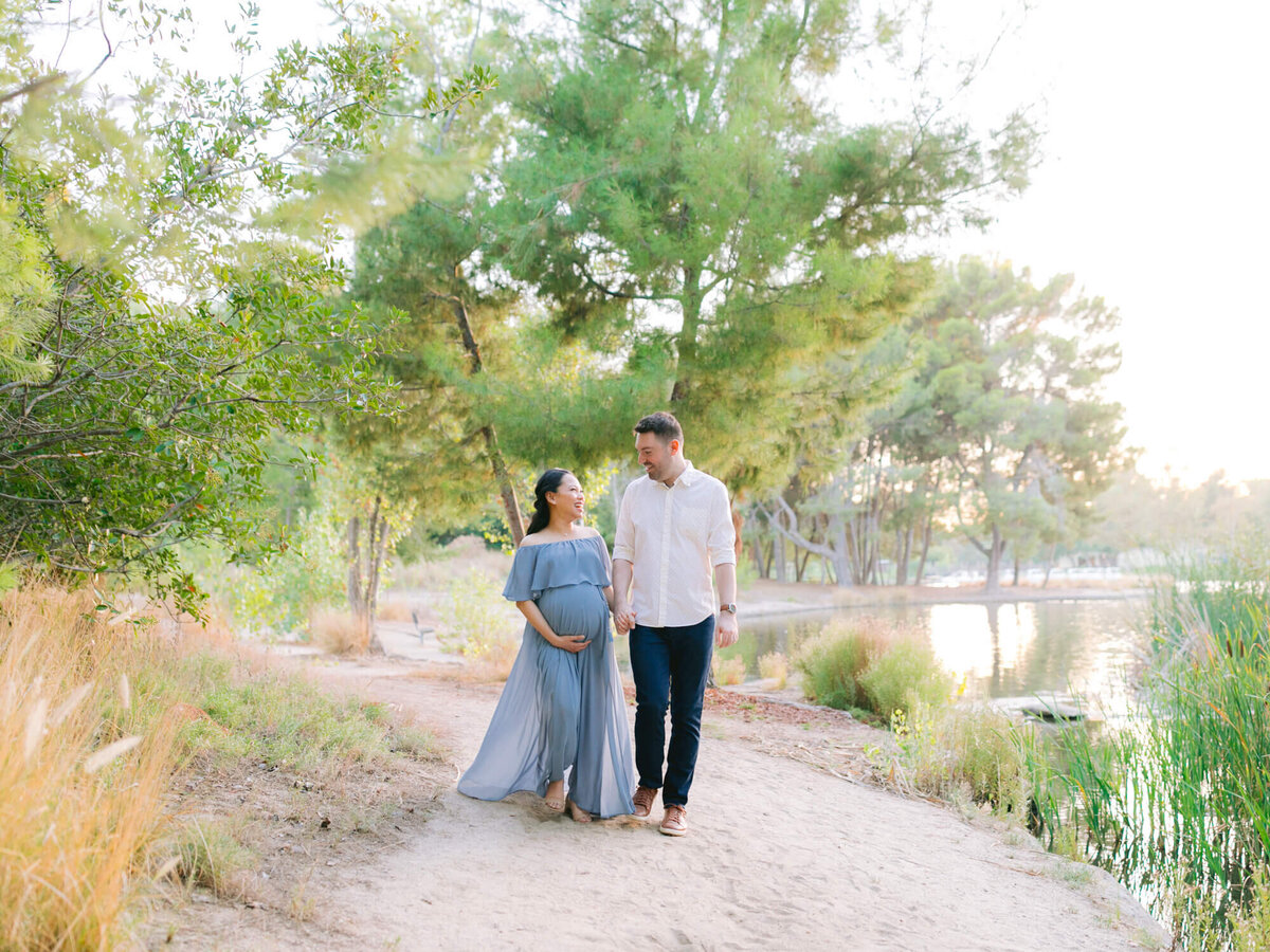maternity photoshoot at yorba linda regional park couple walking on dirt path with lake in the back