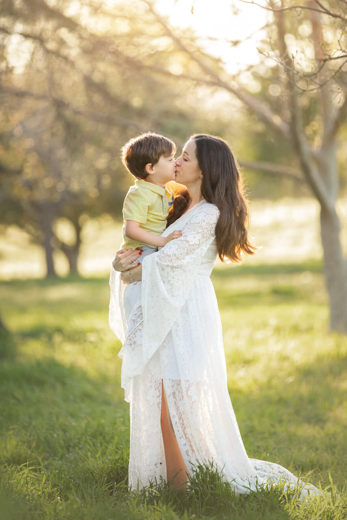 Pregnant mom in a white dress kissing her first born son, captured by Elsie Rose Photography