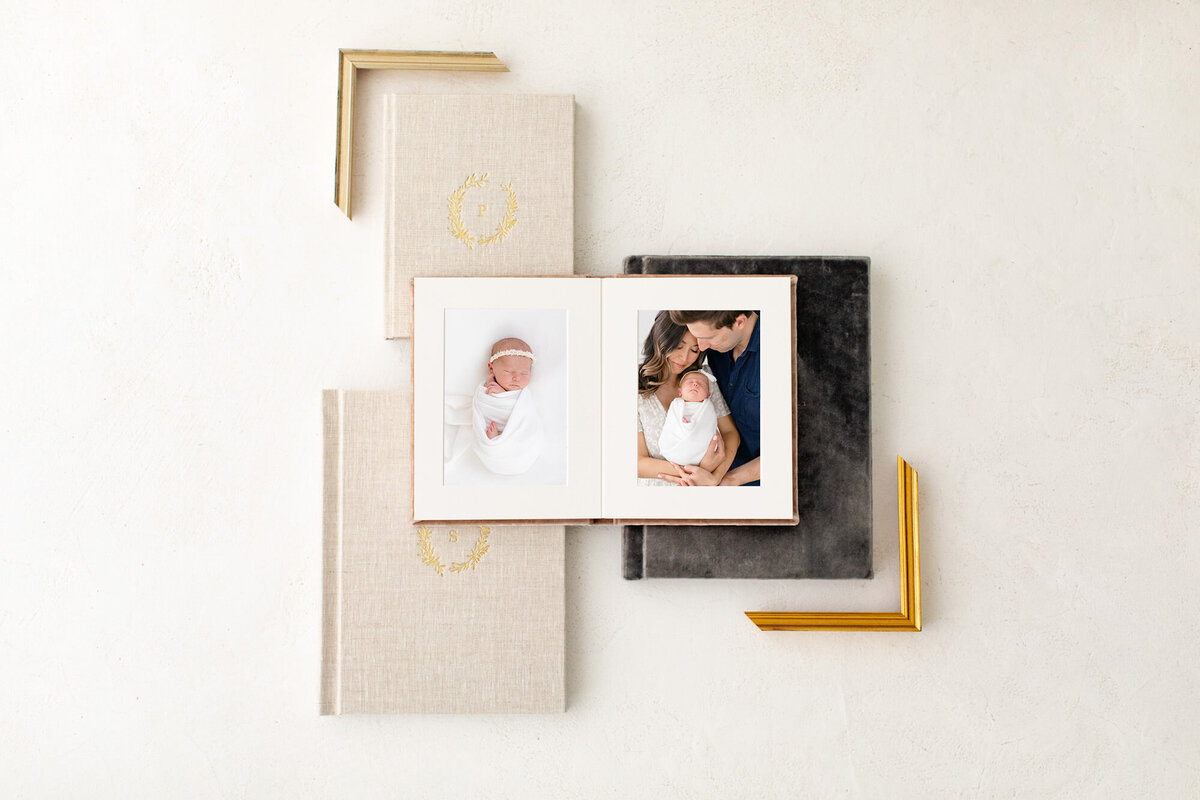 Stack of photo albums with one book open to a page of newborn photos