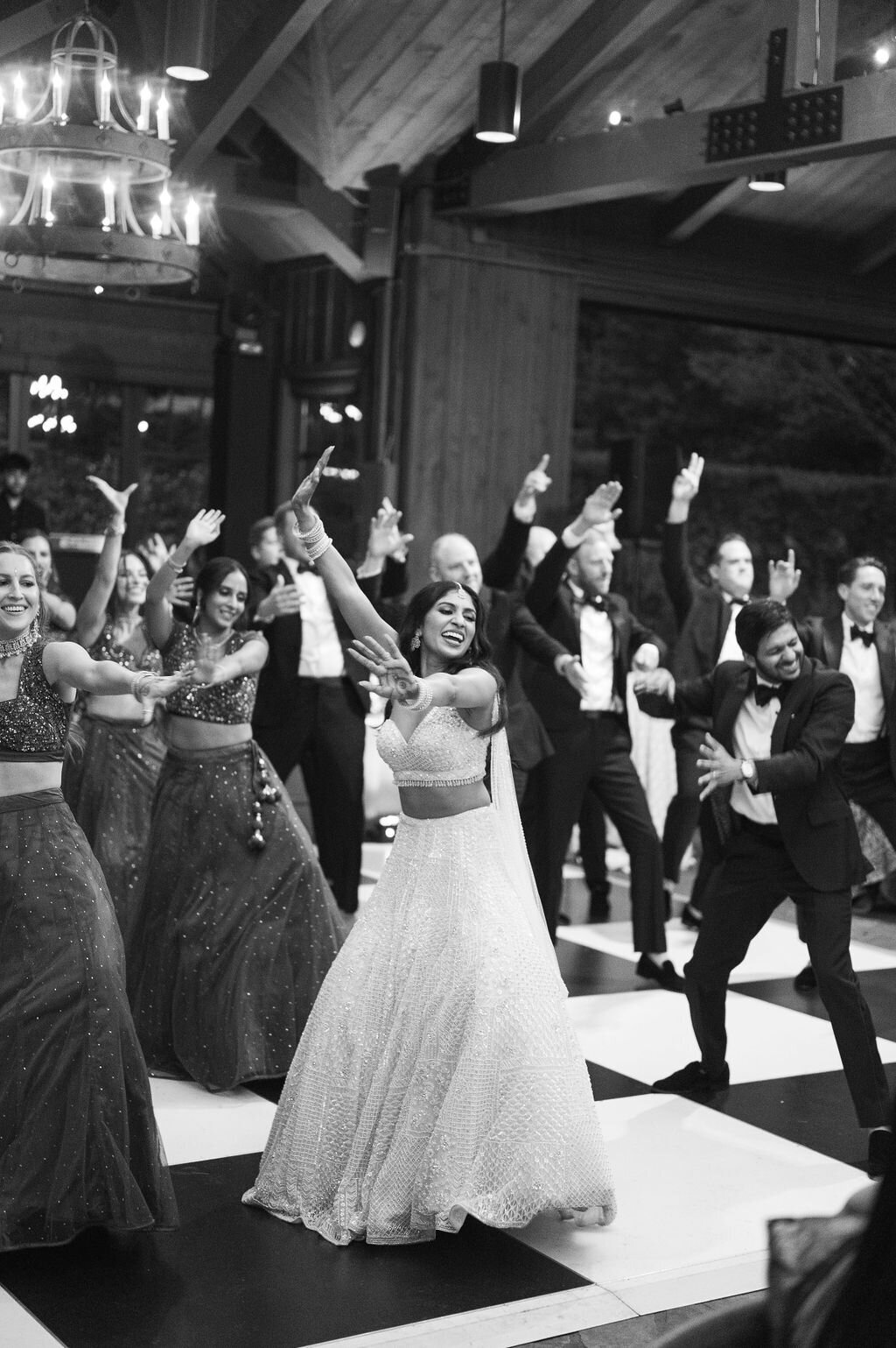 Bride leading a choreographed group dance surrounded by guests beneath chandeliers at a luxury mountain wedding reception.