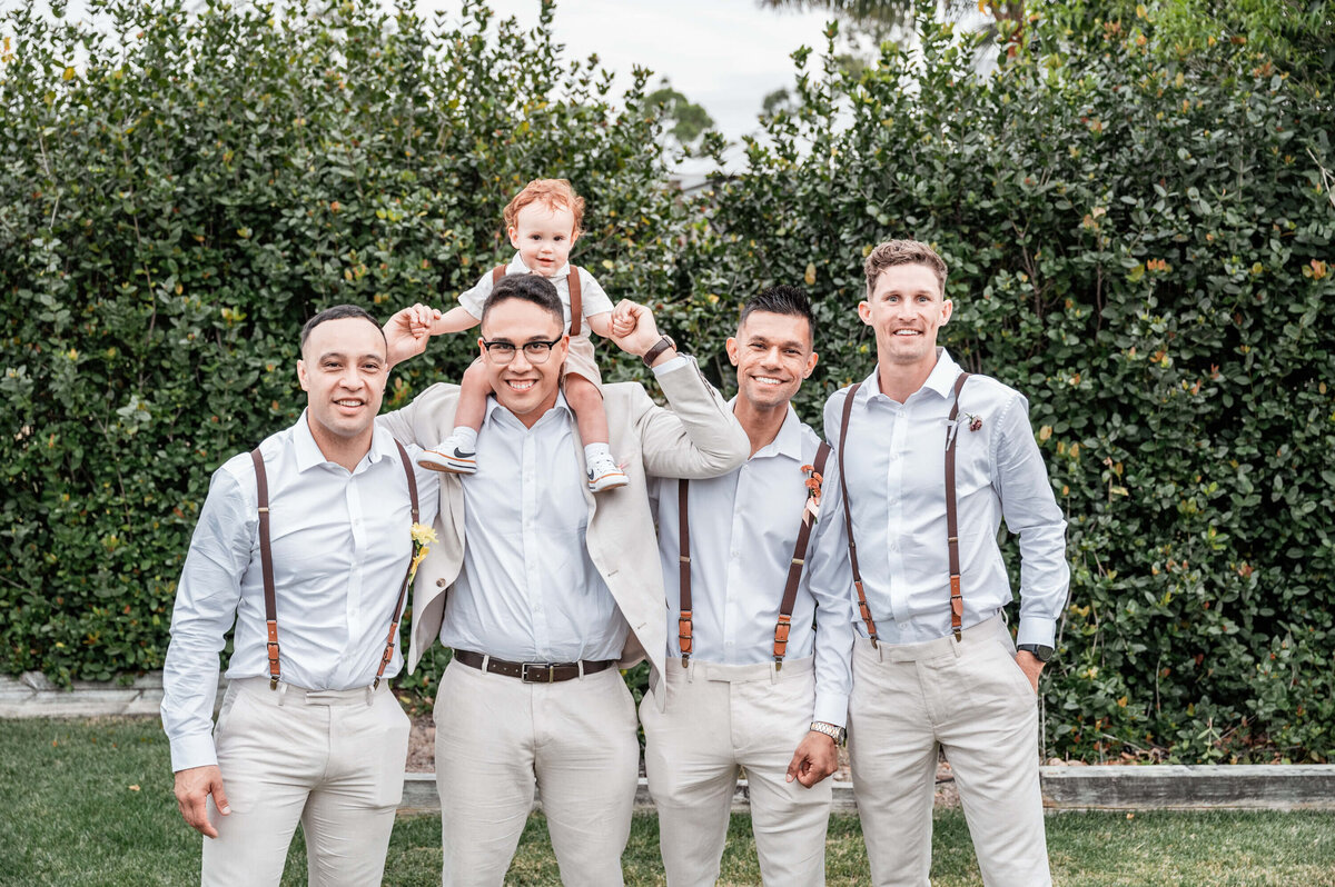 A group of groomsmen poses together with a baby, capturing a heartwarming moment at the wedding. - photo by Jamie Simmons