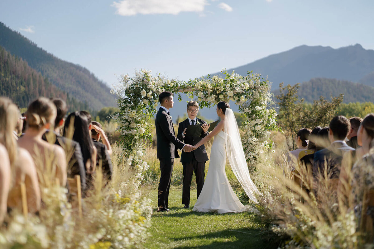 Bride and Groom at the wedding ceremony altar exchange vows with the elegant backdrop of the Aspen Meadows Resort.