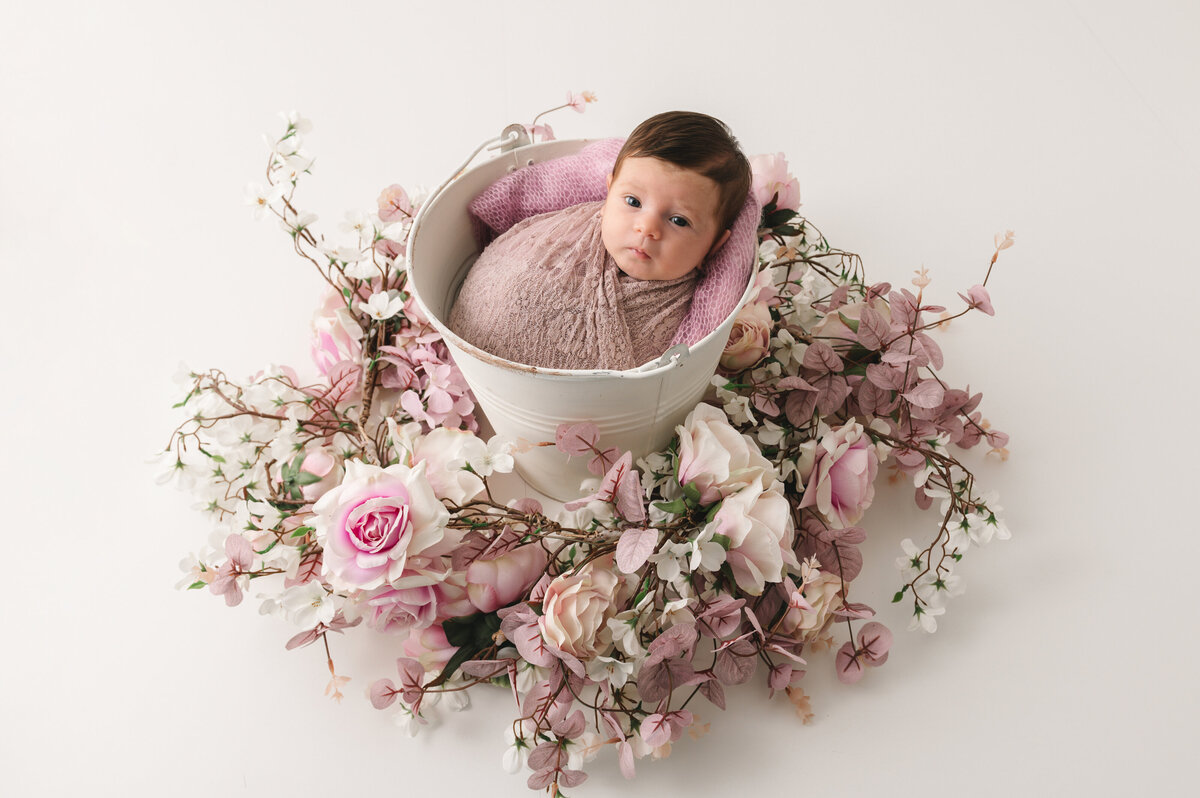 wakker gewrapt baby meisje in een witte emmer omgeven door een witte en roze bloemenkrans
