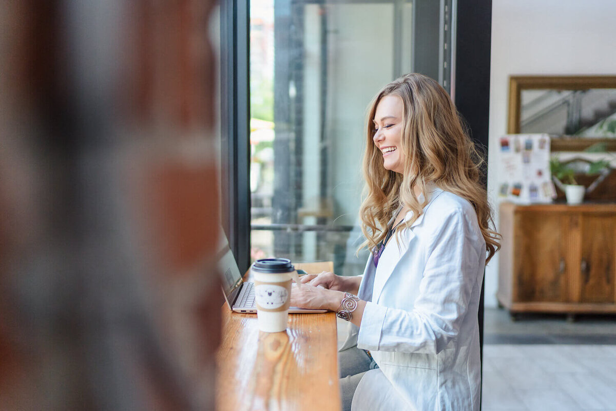 Entrepreneur in white shirt working on laptop at indoor café table, coffee cup nearby.