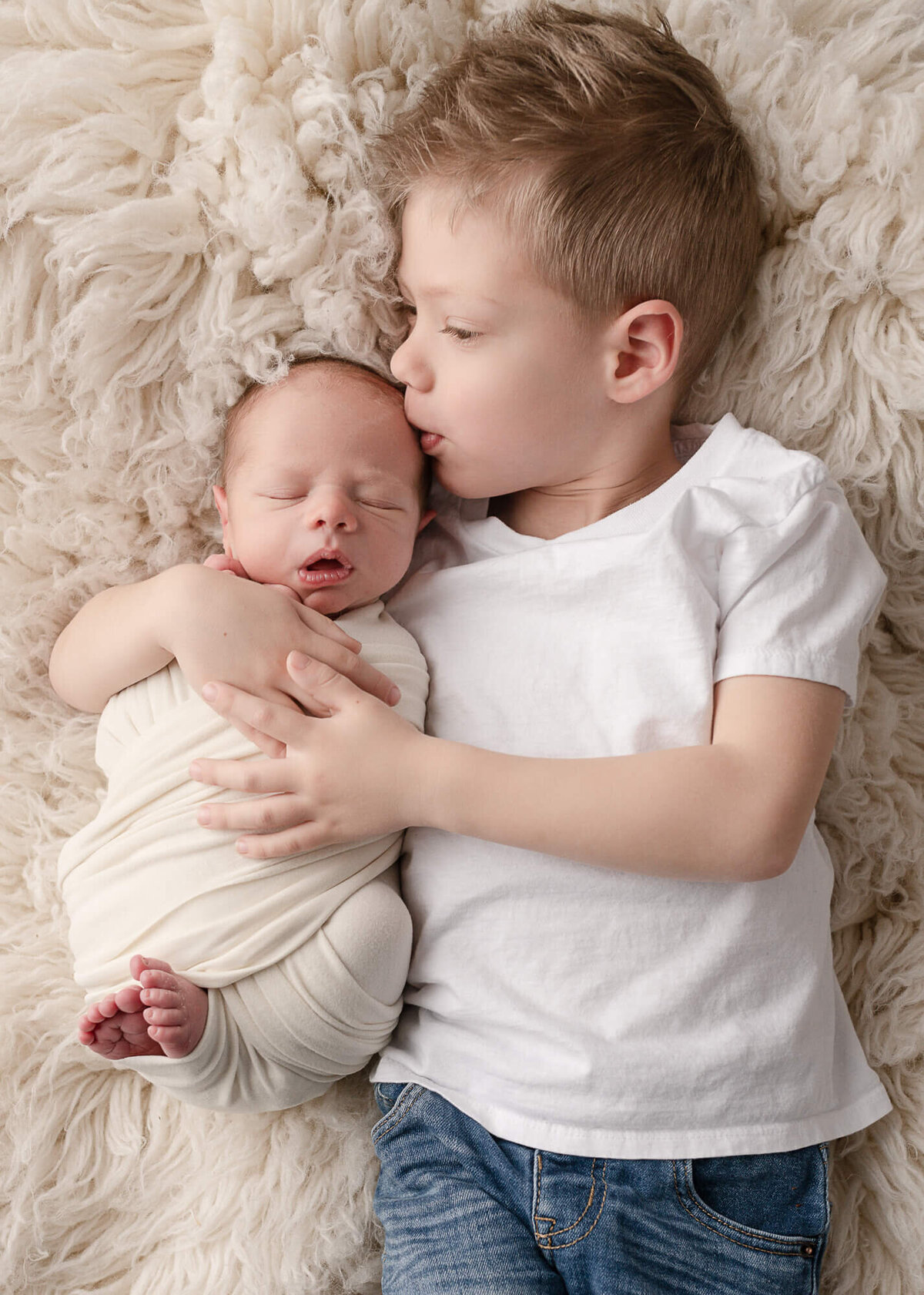 Big brother kissing baby brother on flokati rug